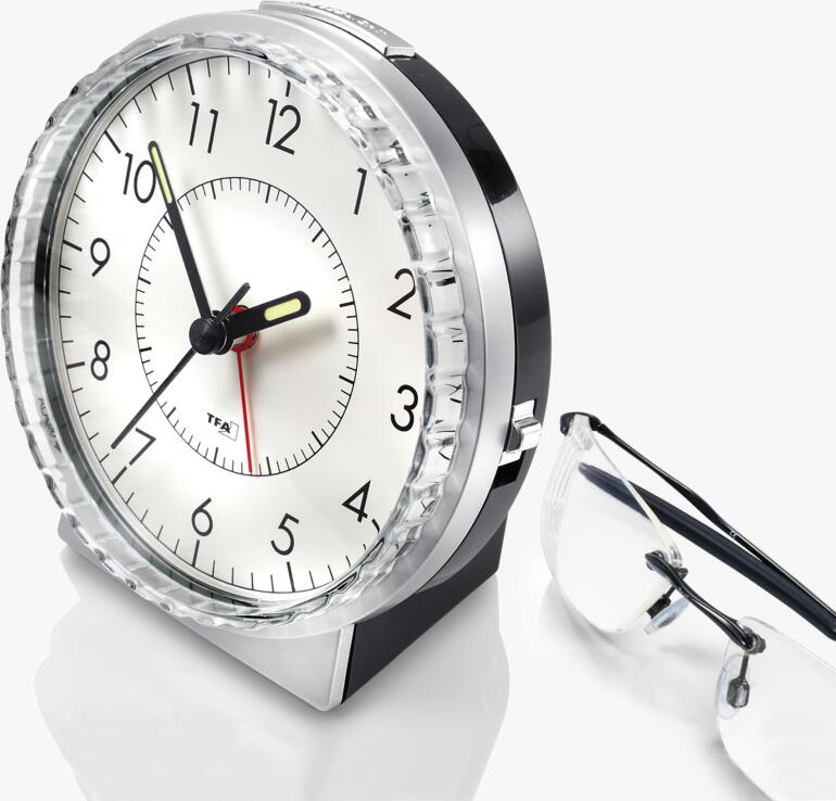 Analoge klok met zwart frame en rode wijzers naast een bril.