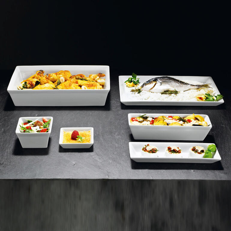Verschillende witte serviesvormen op een donkere tafel, met verschillende gerechten.