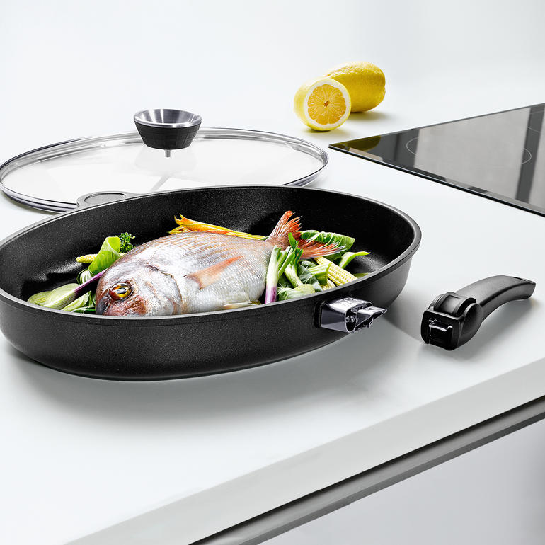 XXL-gietaluminium vispan met vis en groenten op het fornuis.