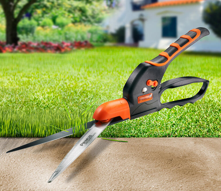 Zijschaar met oranje handgreep knipt grasrand.