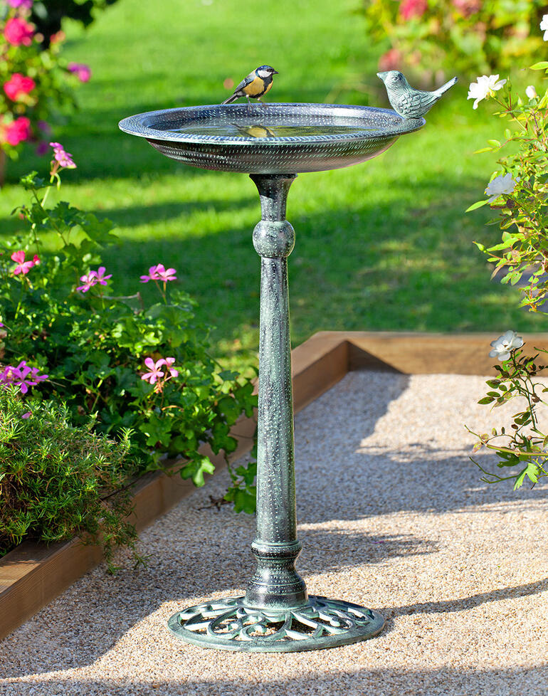 Victoriaans vogelbad met vogel in een bloeiende tuin