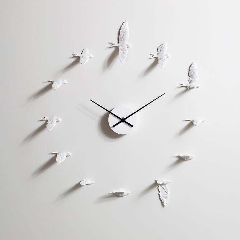 Moderne wandklok in de vorm van zwaluwen, zwarte wijzers op een lichte achtergrond.