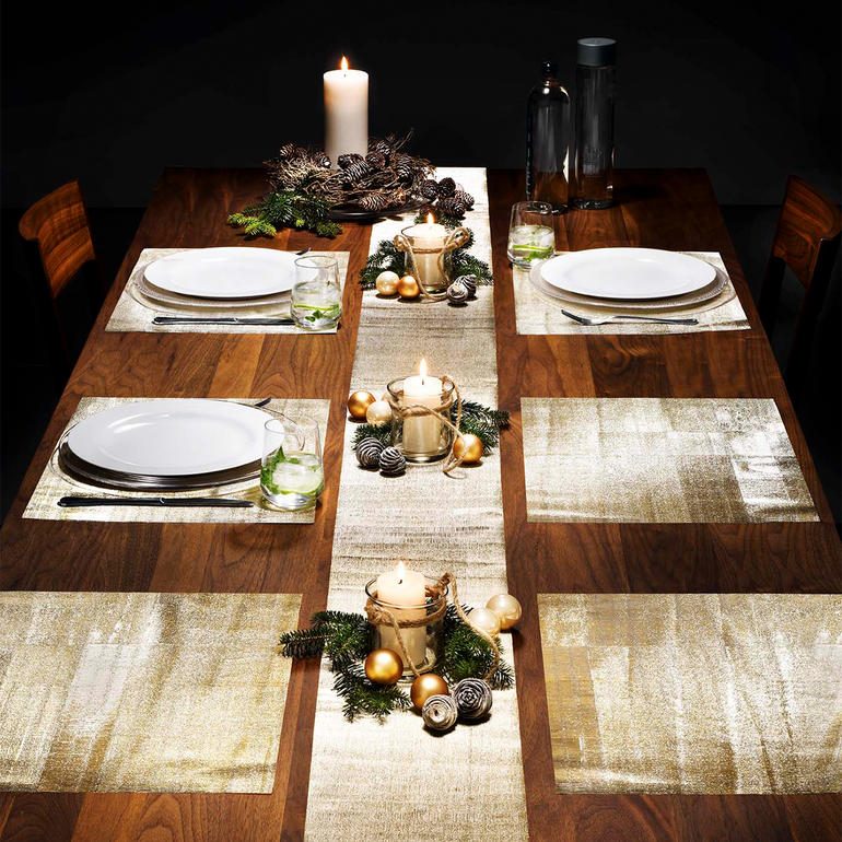 Eettafel gedekt met gouden glinsterende tafelplanken en kaarsen in het midden.