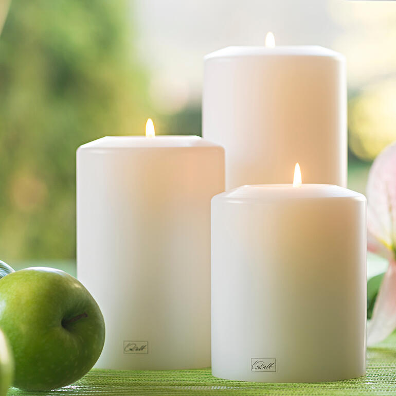 Drie witte duurzame kaarsen in de natuur tussen appels en bloemen