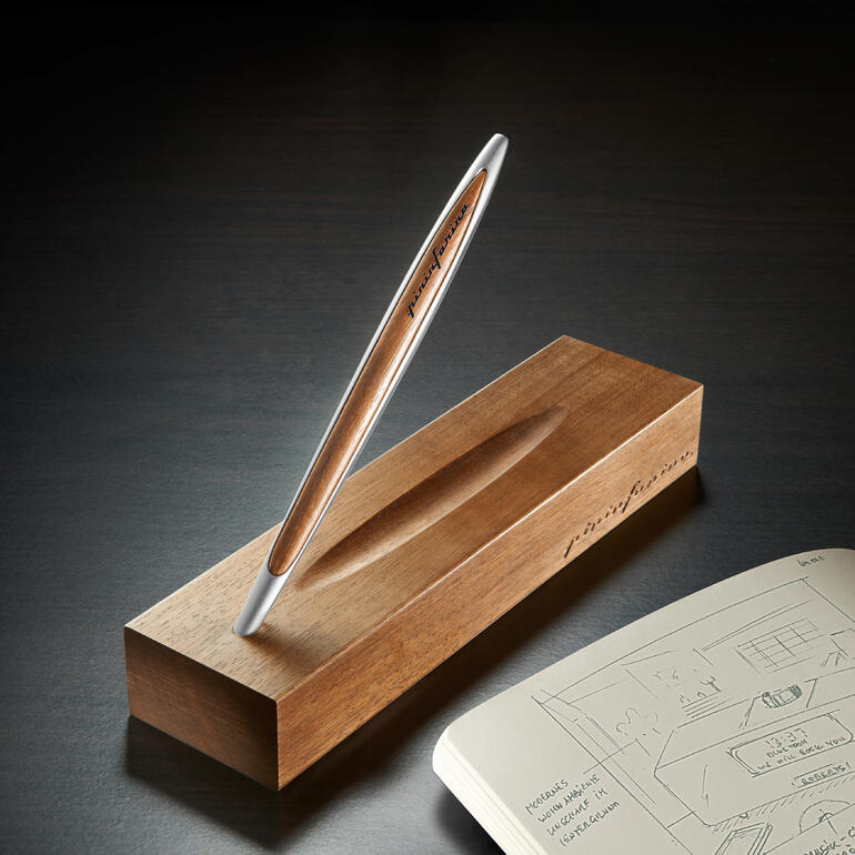 Elegante Pininfarina Ethergraf®-pen op een houten blok naast een notitieboek.