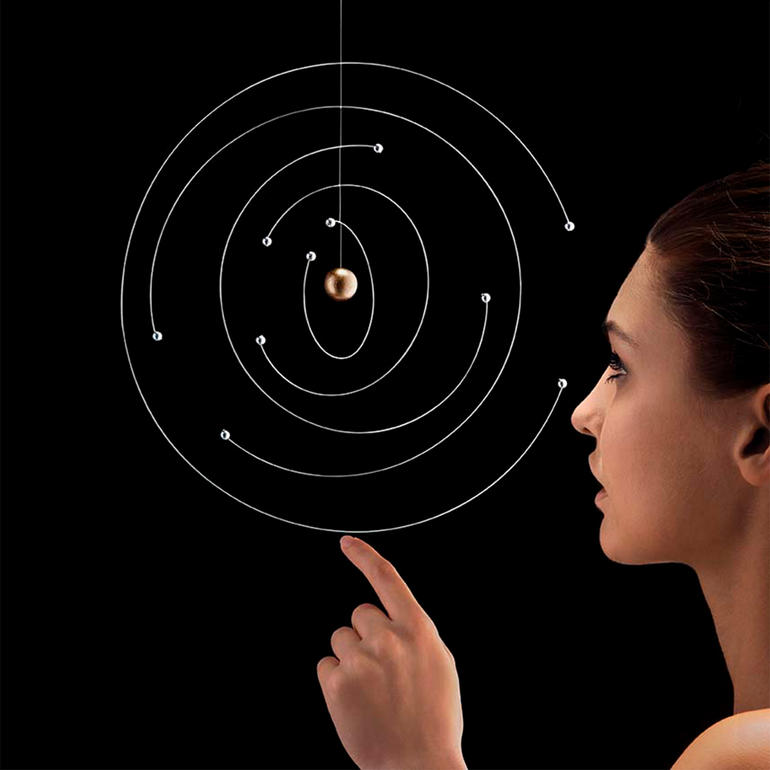 Vrouw wijst naar een zwevend atoommodel met bollen en spiraalvormige banen.