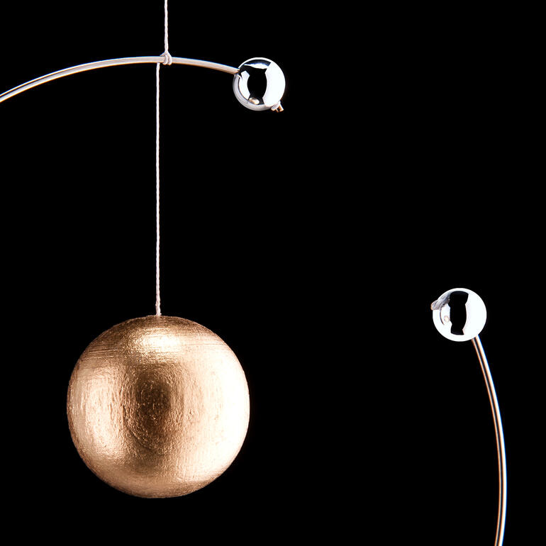 Mobile atoommodel van Niels Bohr Close-up van een gouden bal in het atoommodel, omringd door zilveren elektronen.