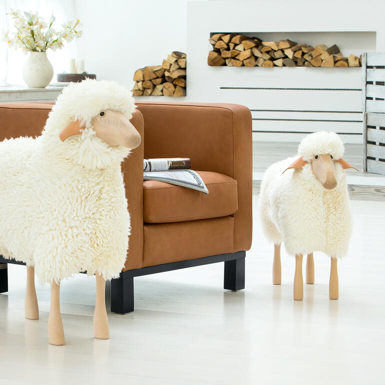 Twee levensgrote schapen van pluche in de woonkamer voor een bank.