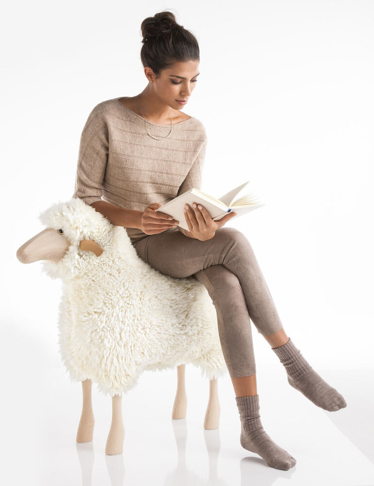 De massief houten basisconstructie is zwaar belastbaar, zodat u het design-object ook als zitplek kunt gebruiken. Vrouw zit op een schaap en leest een boek.