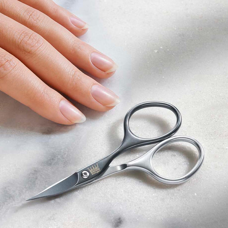 Zelfslijpende manicure-schaar op een tafel naast een hand.