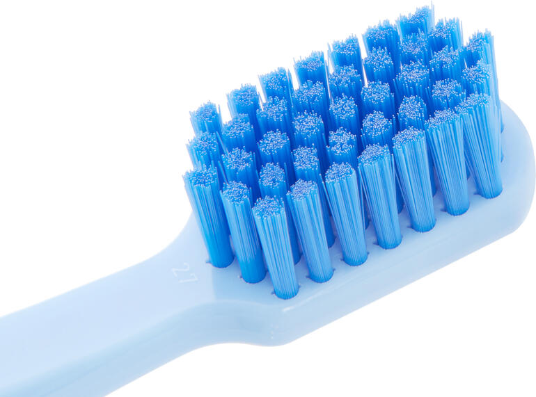 Tandplak en resten worden door de extreem fijne Curen®-filamenten bijzonder grondig verwijderd. Close-up van een witte tandenborstelkop met blauwe haren.