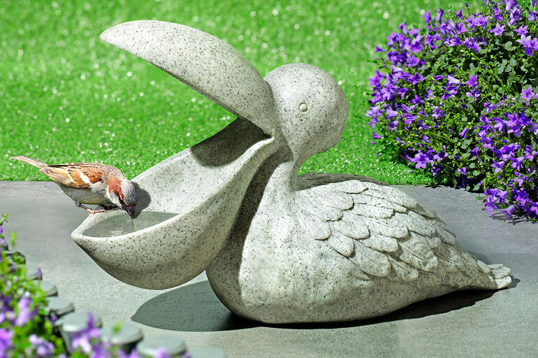 Vogeldrinkbak in de vorm van een pelikaan van steen op groene gras.