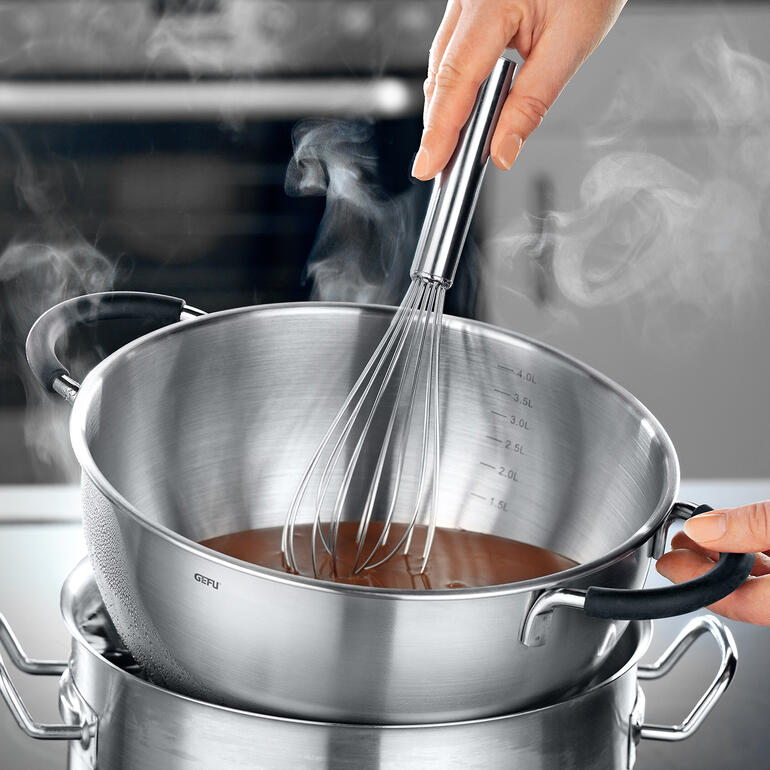 De kom is ideaal om in een waterbad te gebruiken voor het smelten van chocolade. Hand met een garde in een stoomkom boven een au-bain-marie.