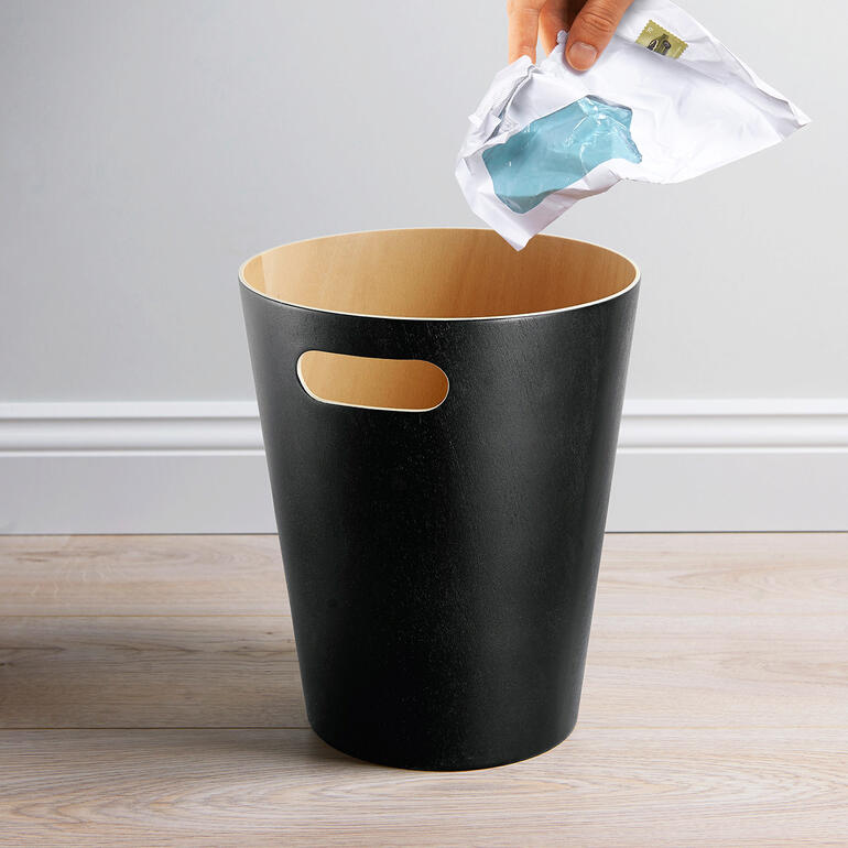 Hand die een plastic tas in een zwarte prullenbak gooit.