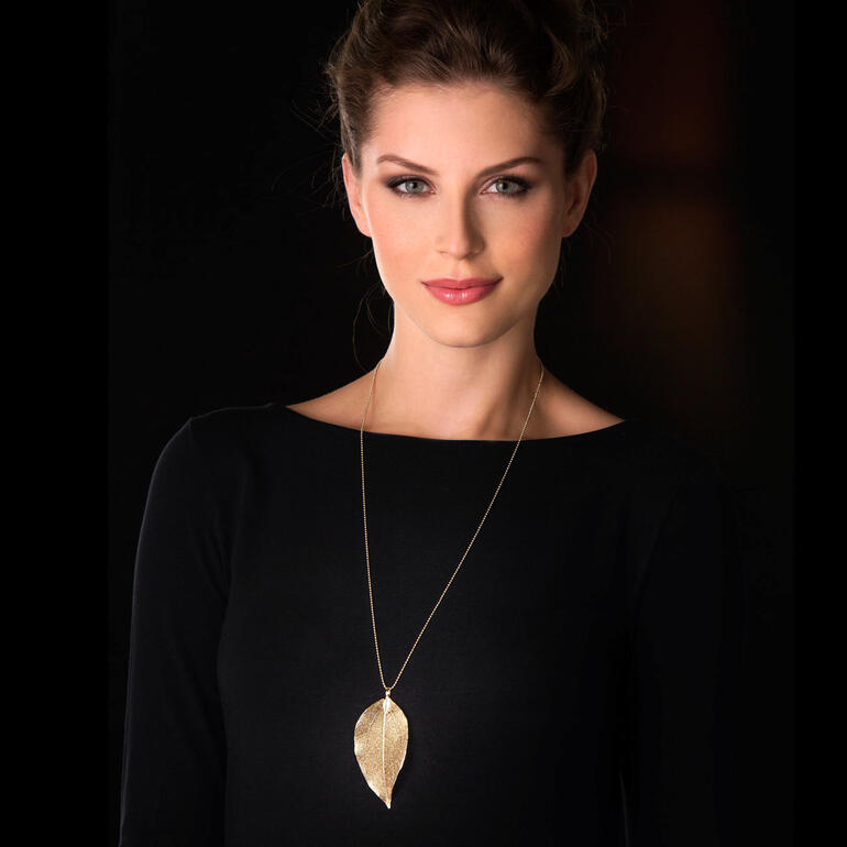 Vrouw draagt gouden Bodhi-bladketting op een zwarte achtergrond.