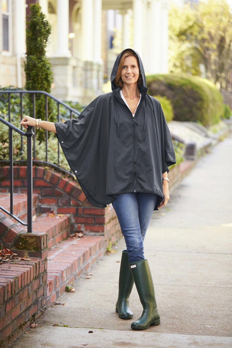 Vrouw draagt een zwarte pocket regenponcho in sportstijl met capuchon, buitenstaand.