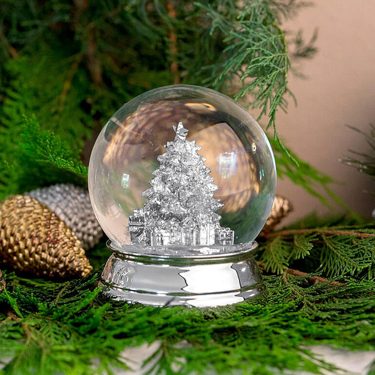 Gesilverde sneeuwbol met een kerstboom erin op groene decoratie