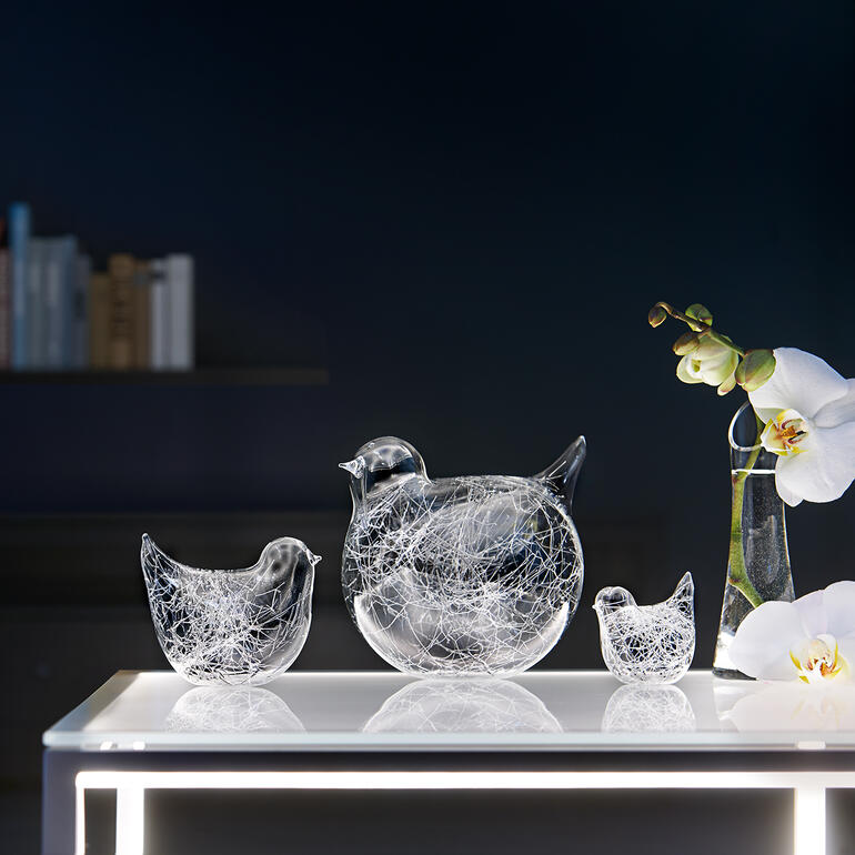 Set van drie glazen vogels decoratief op een tafel, omringd door planten.