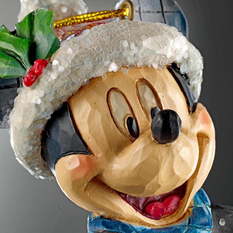 Ziet er kunstig uit, alsof het uit een stuk hout is gesneden. Detail van Mickey Mouse met kerstmute en groene sjaal, blije gezichtsuitdrukking.