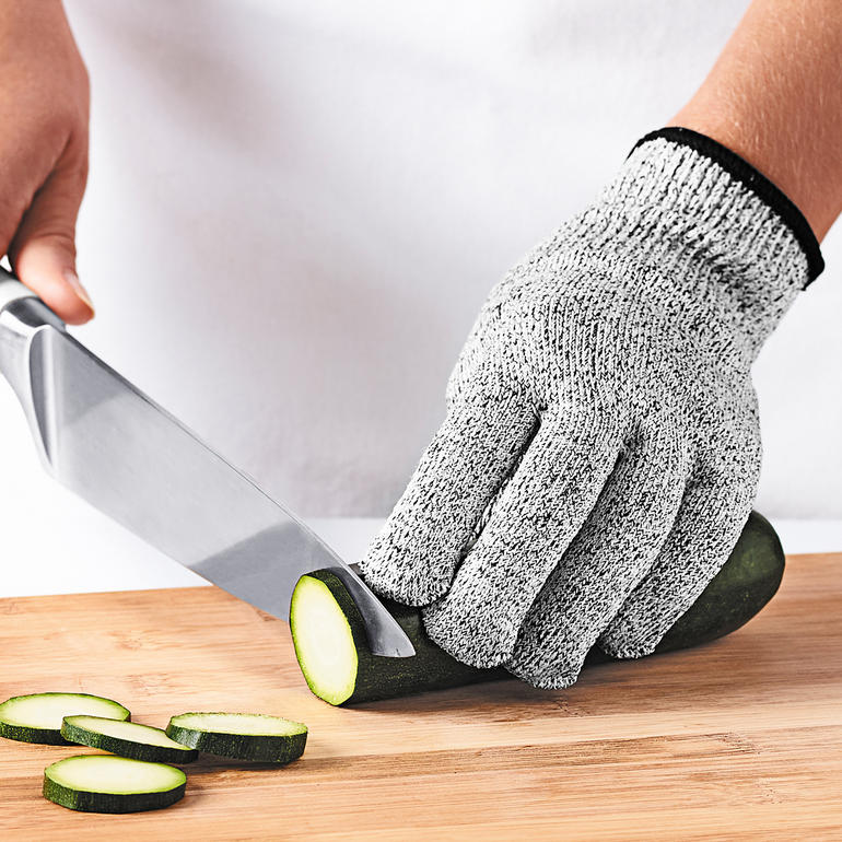 De beweegbaarheid en de tastzin van de vingers blijven behouden. Hand met Mastrad beschermhandschoen snijdt een komkommer op een snijplank.