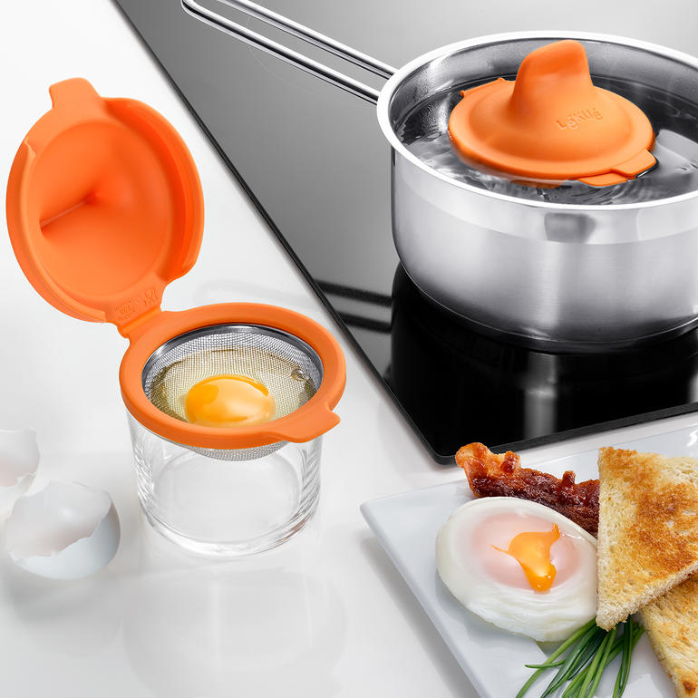 Eipocheerder, set van 2 Oranje eierpocher dicht bij een pan met water op het fornuis.
