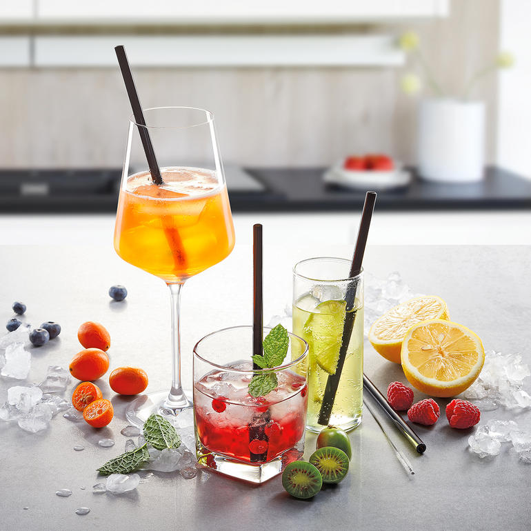 Drie drankjes met glazen drinkhalmen en versierde fruit op een tafeloppervlak.