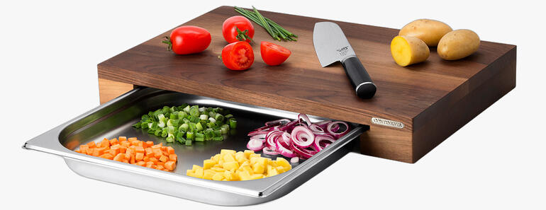 Professionele snijplank van hout met opvangschaal en kleurrijke groenten.