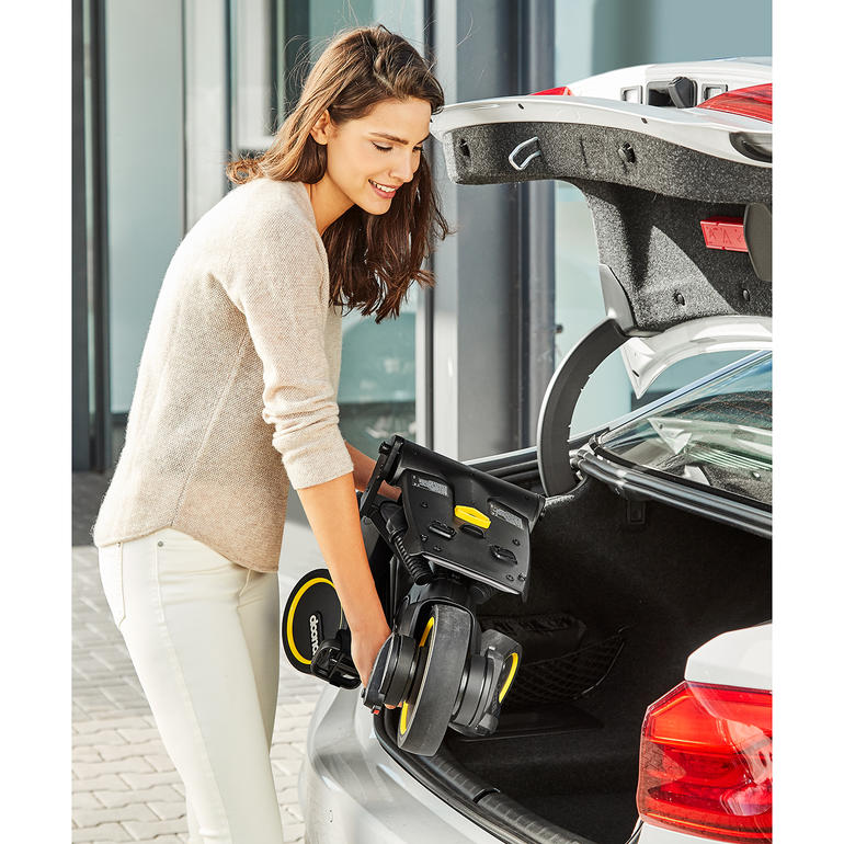 In enkele seconden in te klappen tot het formaat van handbagage. Vrouw heft de opvouwbare driewieler uit de kofferbak van een auto.