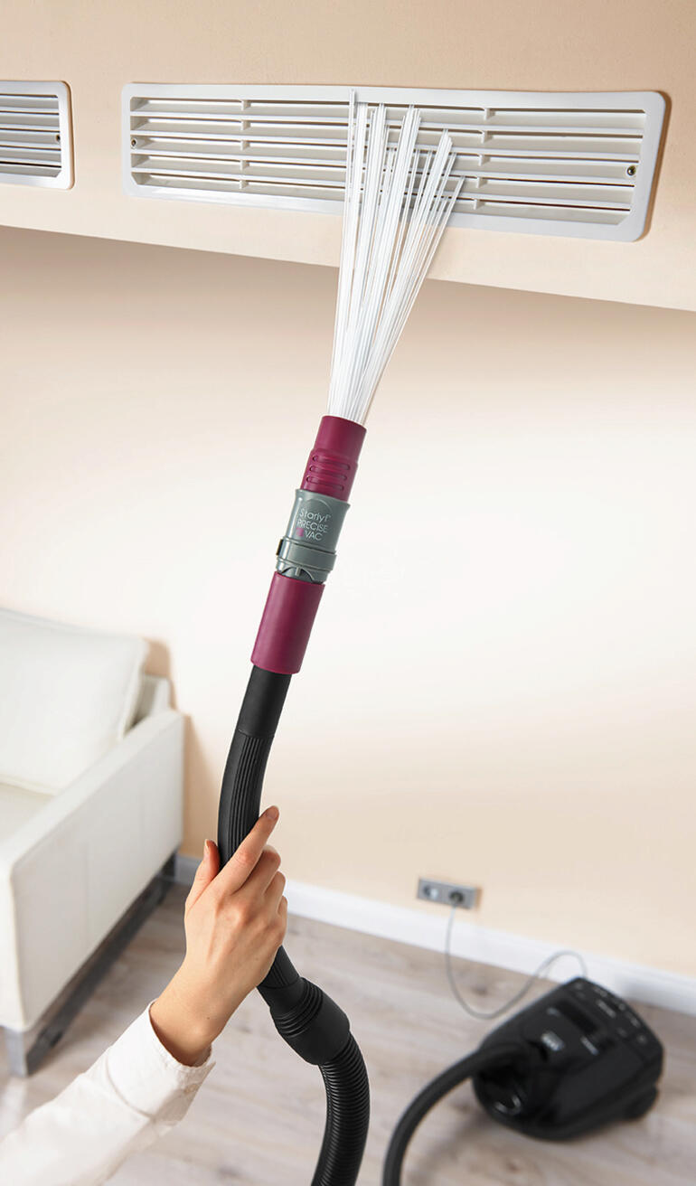 Hand met stofzuigeraccessoire dat een luchtopening schoonmaakt.