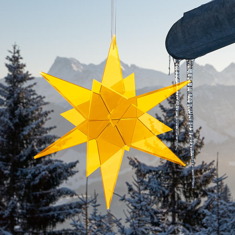 Gele sterren zonnevanger hangt aan een dakrand met besneeuwd landschap