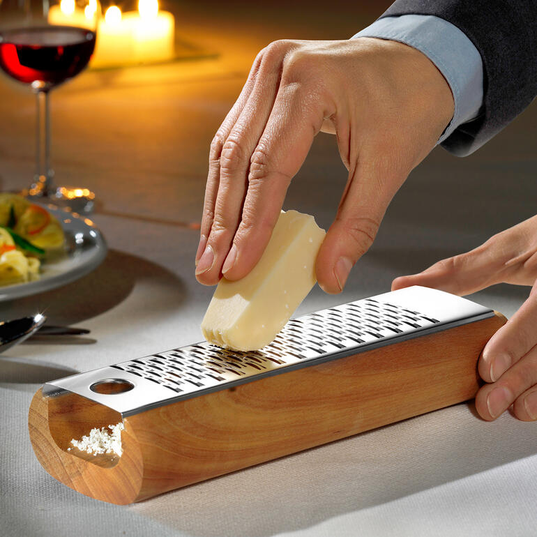 Man raspt kaas op een houten designkaasschaaf.