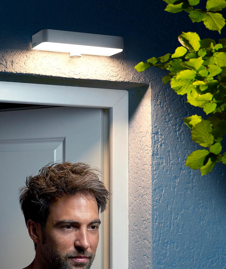 Man staat onder een buitenwandlamp bij de deur.