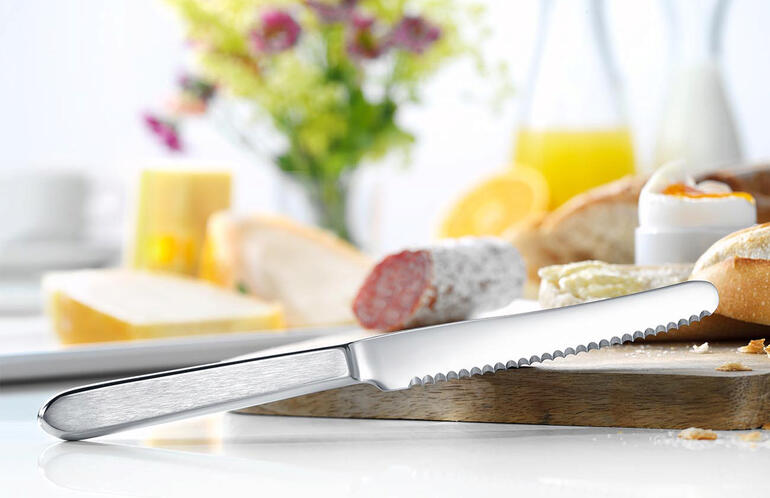 Broodmes van roestvrij staal op een tafel met brood en bloemen.