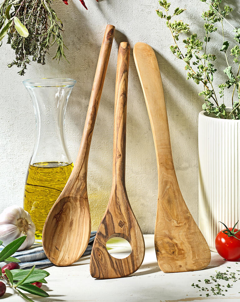 Drie-delig olijfhouten keukengerei op een rustieke tafel met kruiden.