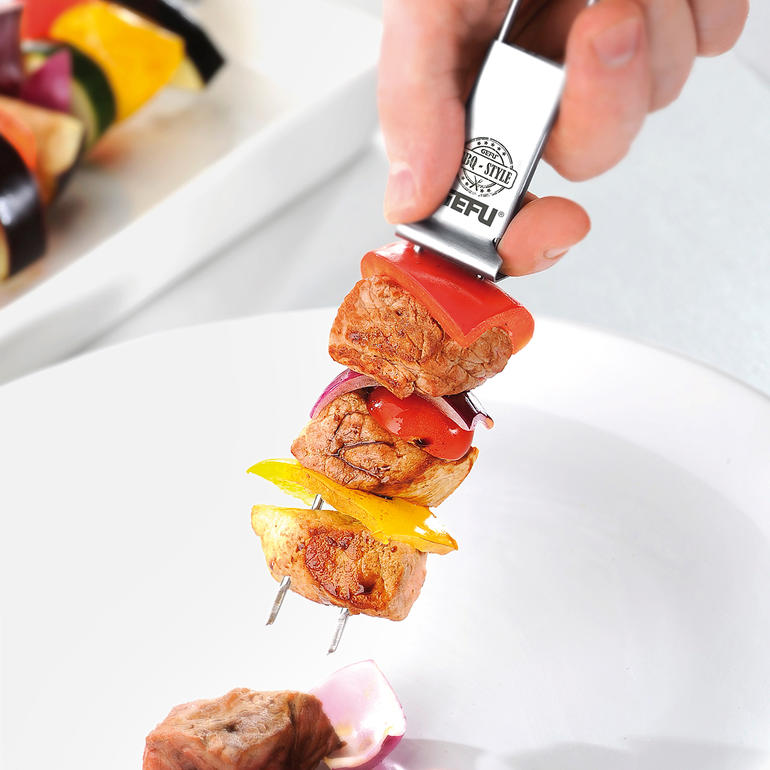 Hand met een dubbele grillspiezen, belegd met groenten en vlees