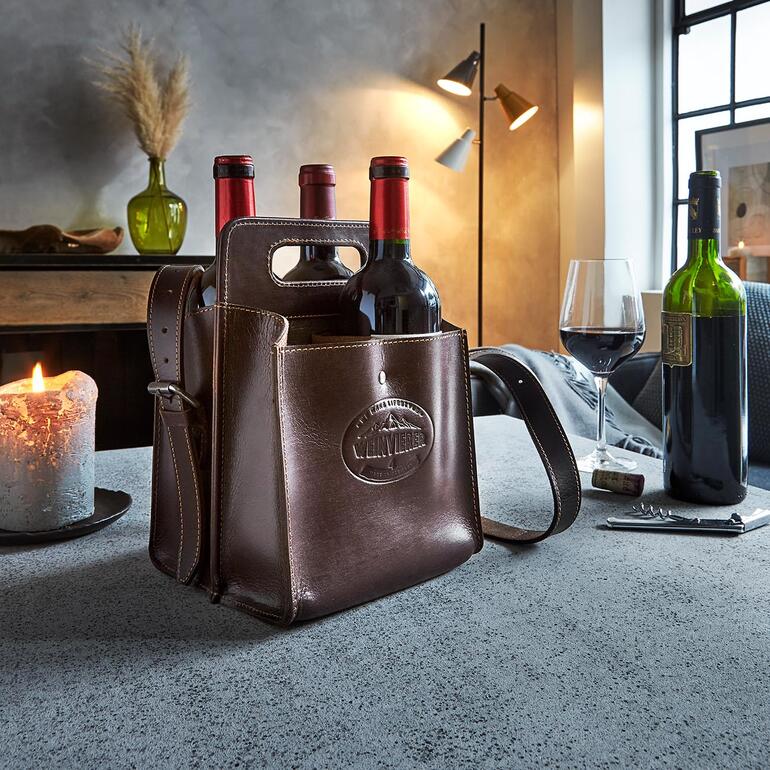 In de ‘Weintragerl’ kunt u 4 flessen van elk 0,7 l meenemen. Buffelleder flessenhouder met wijnflessen, op een tafel in een stijlvolle ruimte