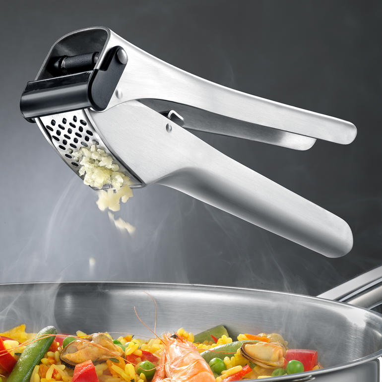 RVS knoflookpers boven een pan met kleurrijke groenten