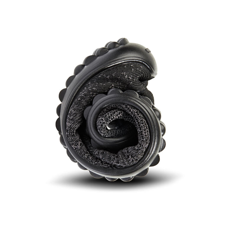 Slechts 8 mm dun en zeer buigzaam: noppenzool van Lifolit®. Opgerolde zwarte Barfuß-leguano® Knit-Sneaker, compact opgevouwen.