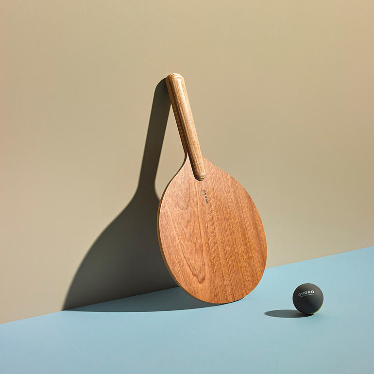 Houten beachball racket met zwarte bal op een blauwe ondergrond.