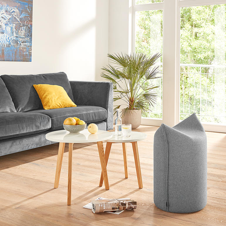 Puntige pouf in grijze stof in woonkamer met bank en tafel.