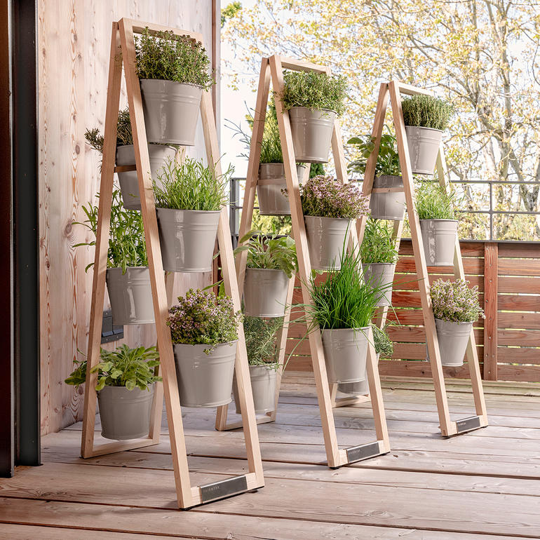 Wanneer u hem gespreid plaatst, blijft de houten ladder op elke vlakke ondergrond stabiel staan. Drie houten plantenladders met potten buiten op een houten terras
