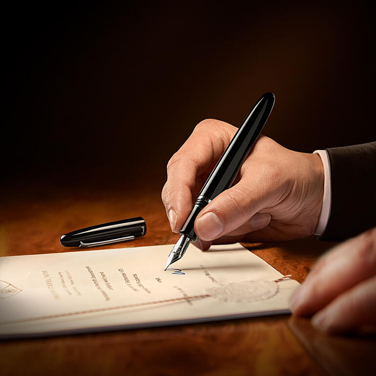 Esterbrook vulpen in de hand van een man terwijl hij op een document schrijft.
