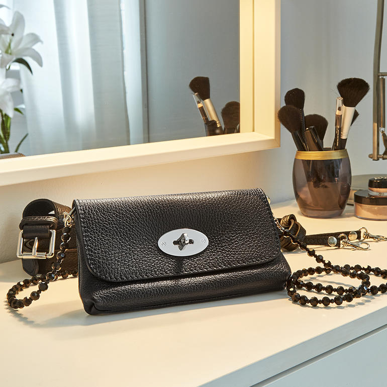 Zwarte leren heuptas op een make-uptafel, met cosmetica.