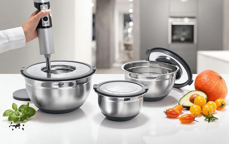 Drie roestvrijstalen kommen in verschillende maten met keukenhulpmiddelen op een werkblad.