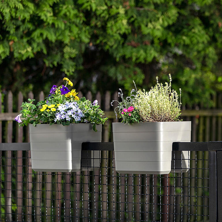 Twee hangende bloempotten met verschillende kleurrijke bloemen op een balkon.