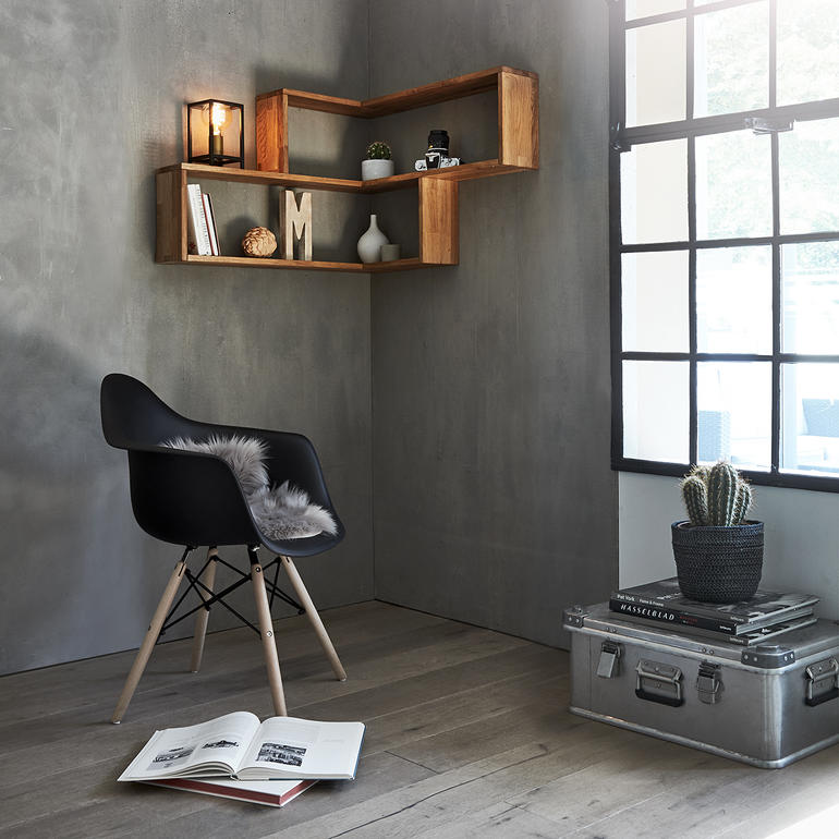 Houten wandhoekrek met decoratieve objecten en een zwarte stoel in een kamer.