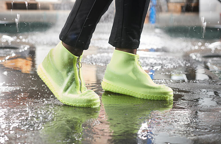 Persoon met lichtgroene regenoverschoenen staat in een plas.