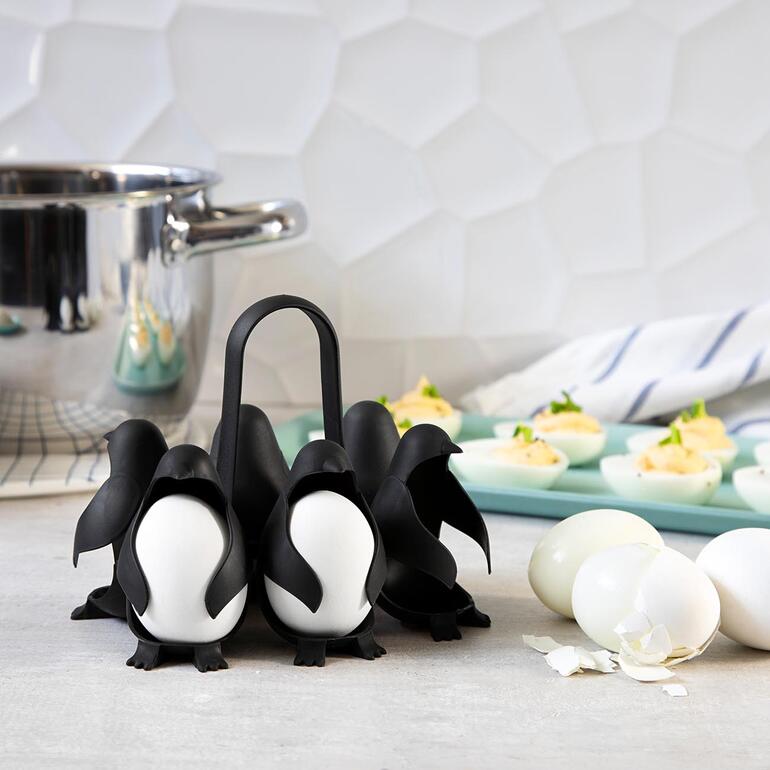 Eierhouder in de vorm van pinguïns met gekookte eieren en een potdecoratie op de achtergrond.