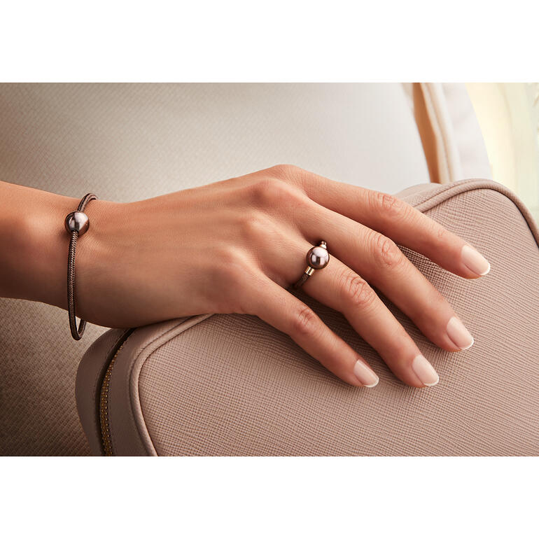 ring en klemarmband Hand die een roségouden armband en ring met zwarte parel op een tas houdt.
