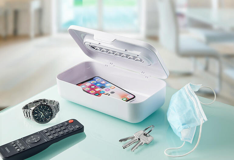 UV-C-straalsterilisator 2-in-1 met smartphone en dagelijkse voorwerpen op een tafel.